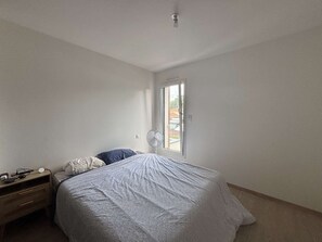 Een slaapkamer met een bed, nachtkastje, ventilator en raam.