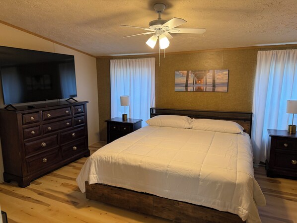 A hotel room with a bed, a dresser, a television, a ceiling fan, and a painting on the wall.