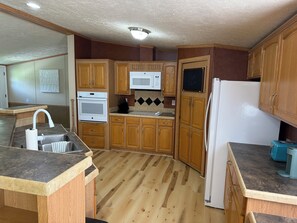 A compact kitchen with wooden cabinets, a white microwave, a built-in oven, and a refrigerator.