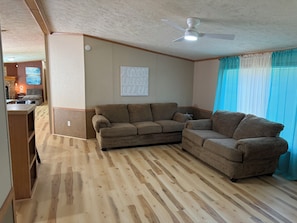 A living room with a wooden floor, two sofas, a ceiling fan, and a window with curtains.