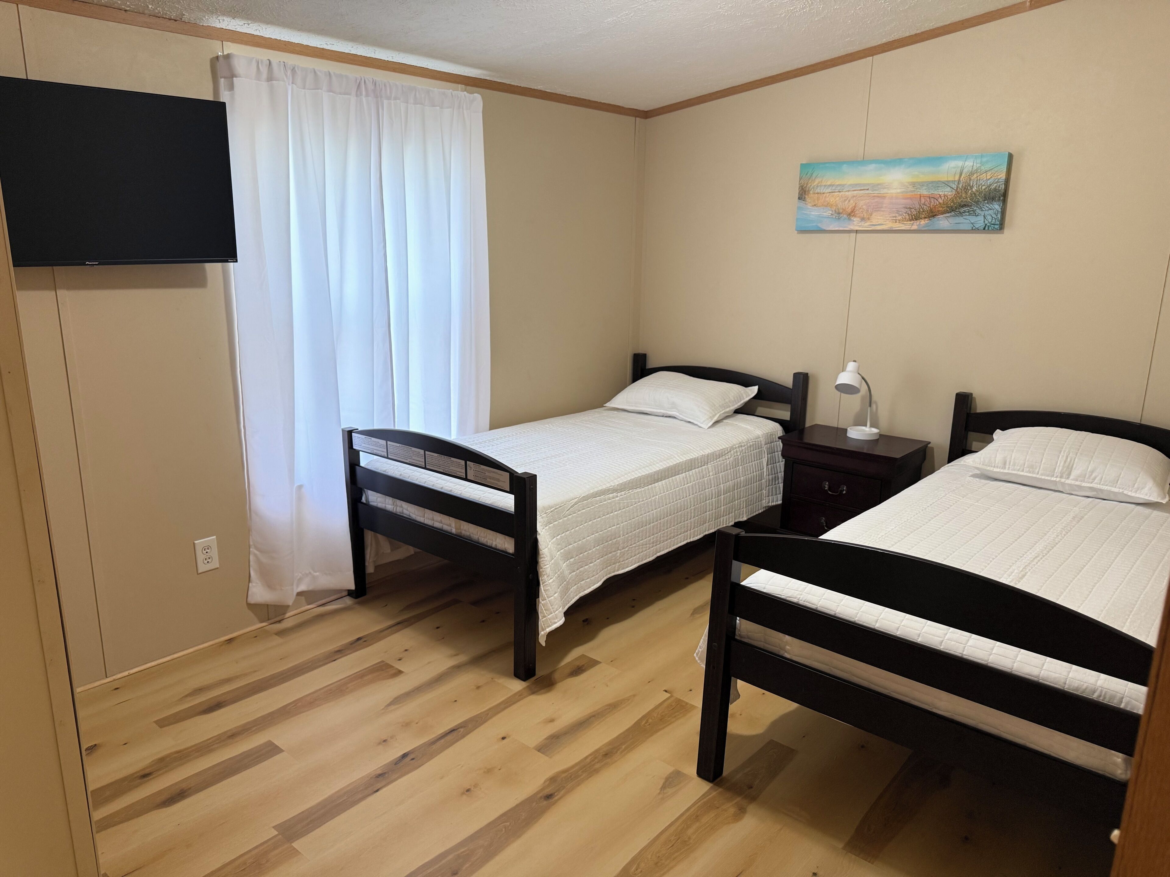 Une chambre avec deux lits en bois, un téléviseur à écran plat fixé au mur et un tableau au-dessus des lits.