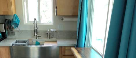 A kitchen with wooden cabinets, a stainless steel sink, a window with curtains, and a wooden dining table with two chairs.