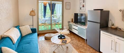 A compact living space with a sofa, a small coffee table, a kitchen area with a refrigerator, and a dining area with chairs and a table.