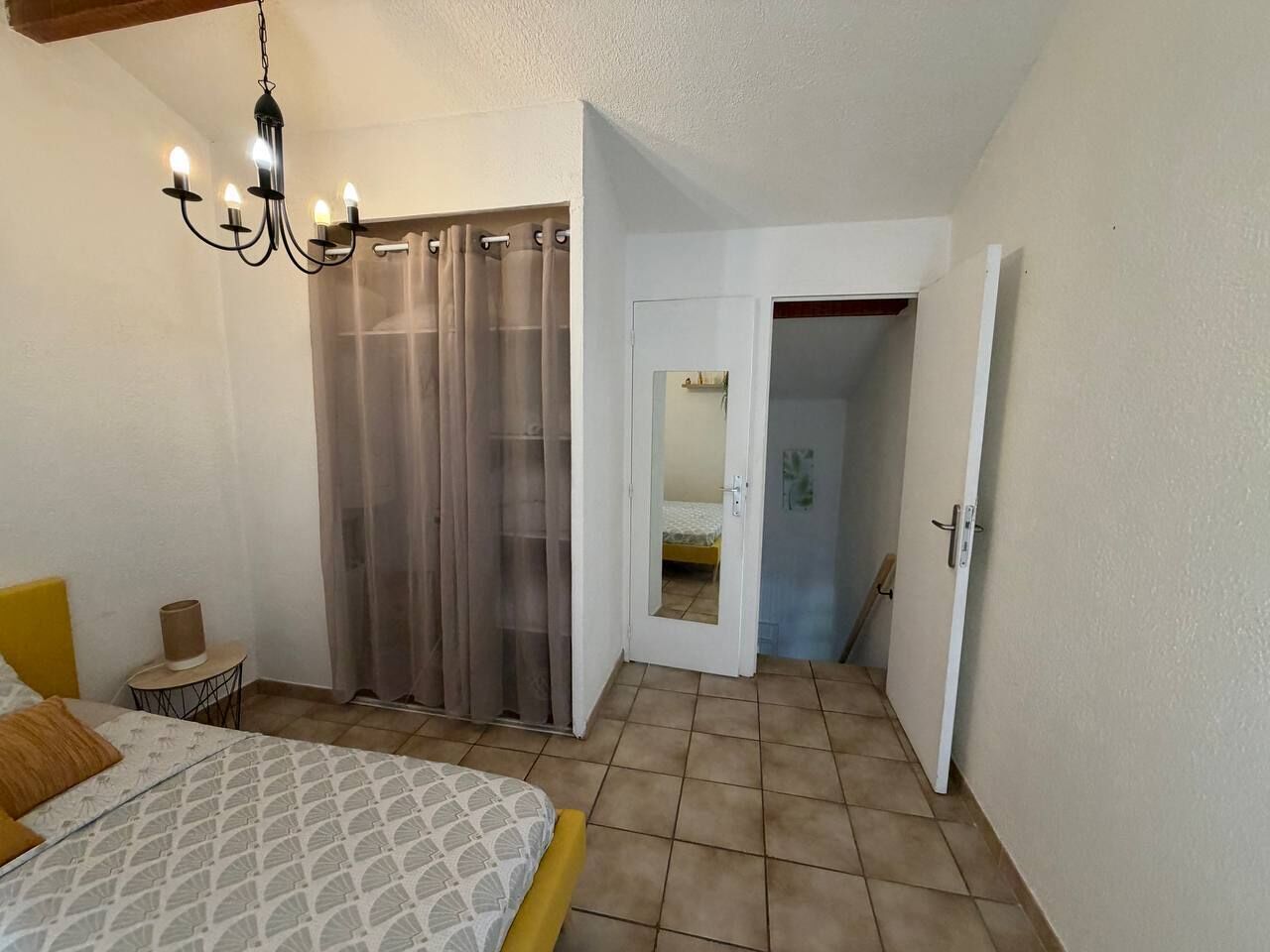 A bedroom with a bed, a bedside table, a chandelier, a closet with a sliding door, and a door leading to a bathroom.