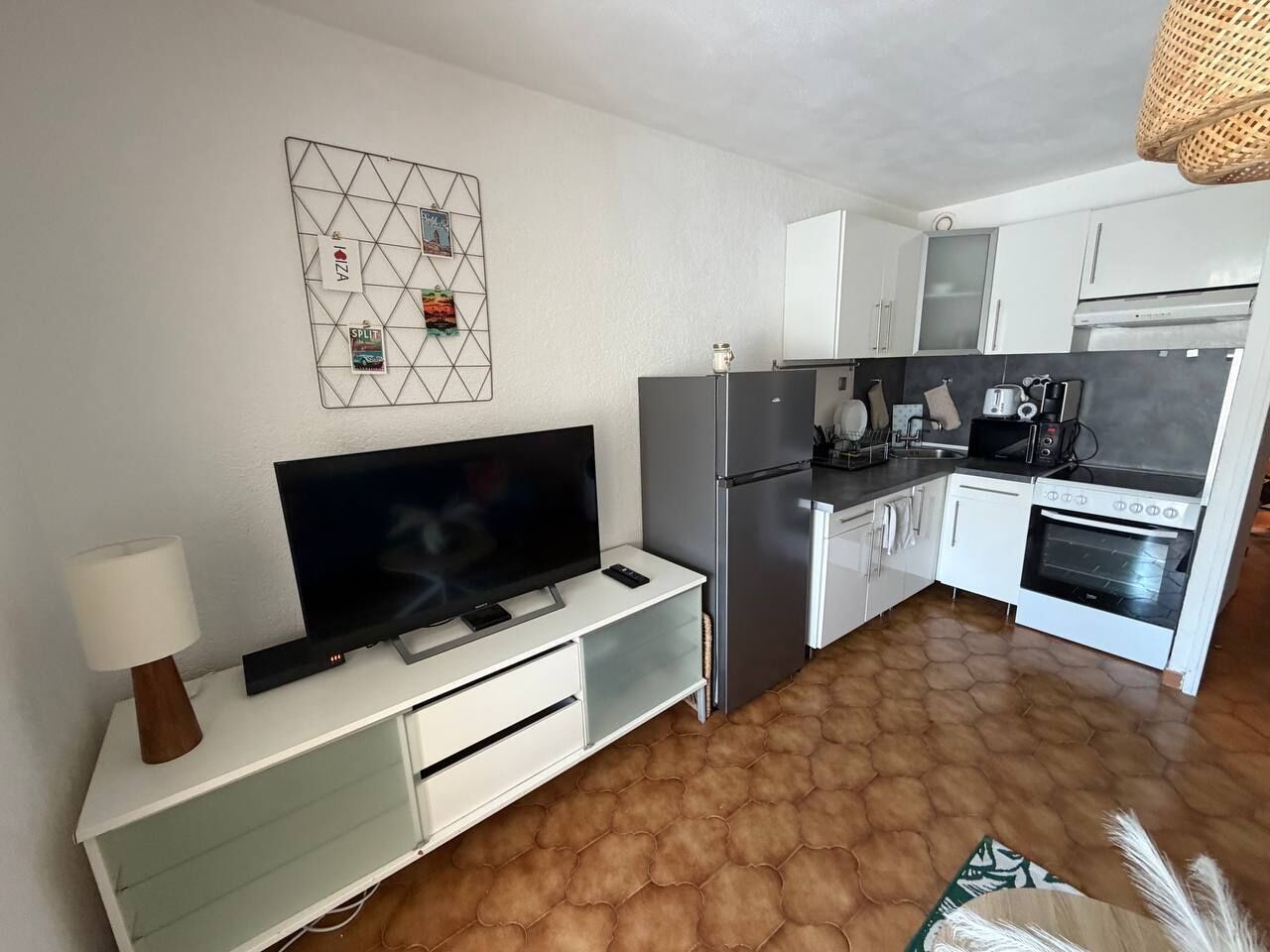 Eine moderne Küche mit Flachbildfernseher, weißen Schränken, einem Kühlschrank und einem Herd.