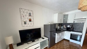 Eine moderne Küche mit Flachbildfernseher, weißen Schränken, einem Kühlschrank und einem Herd.