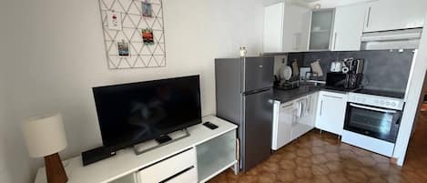 Eine moderne Küche mit Flachbildfernseher, weißen Schränken, einem Kühlschrank und einem Herd.