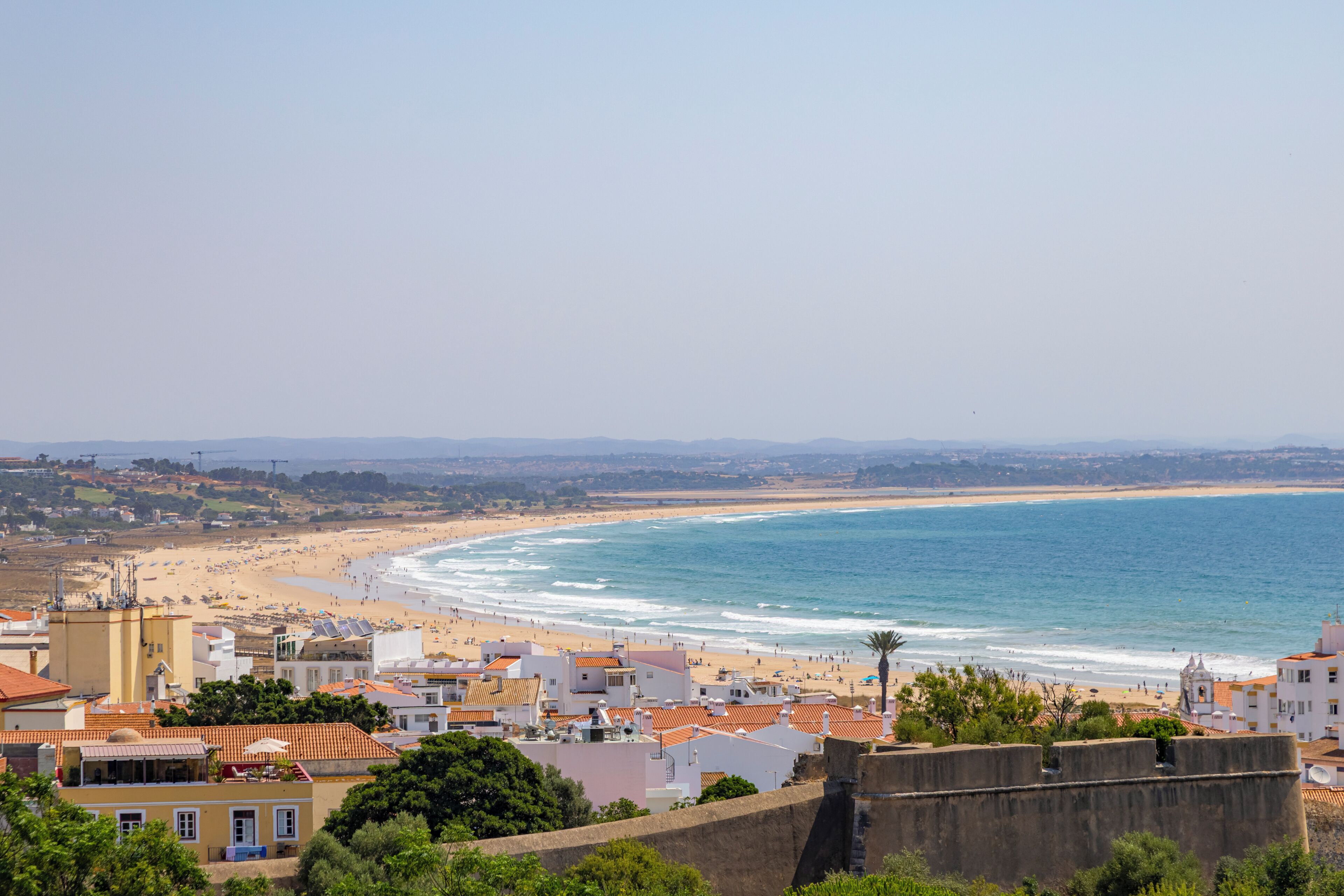 Une ville côtière dotée d’une plage, de bâtiments aux toits recouverts de tuiles rouges et offrant une vue dégagée sur la mer.