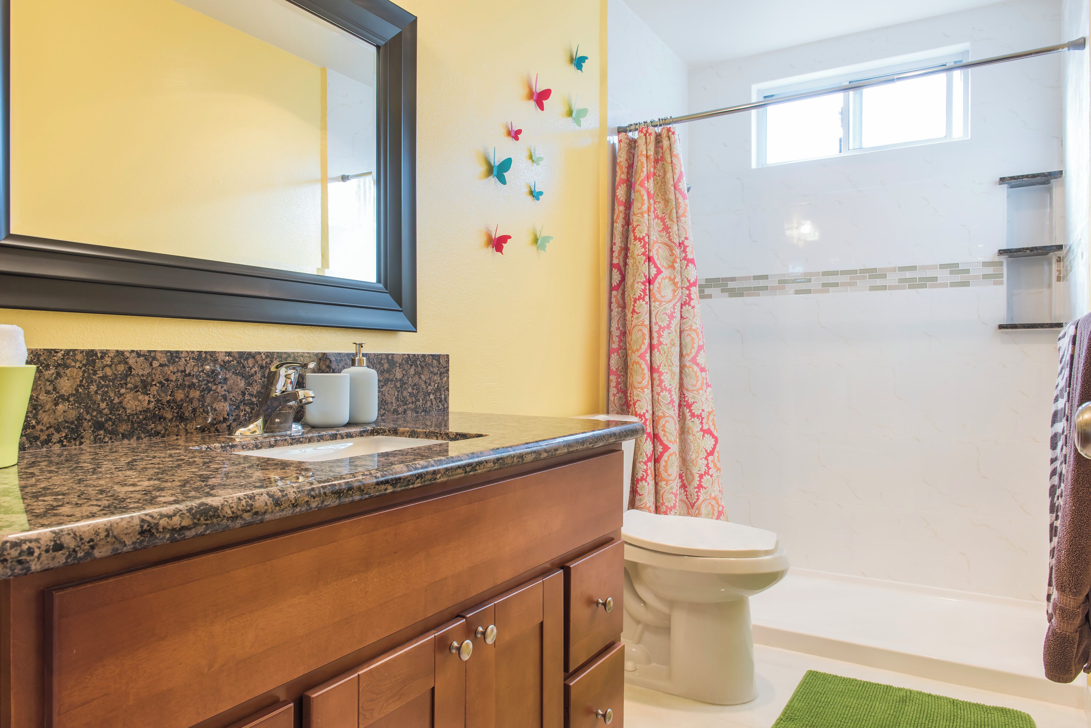 Une salle de bain avec un comptoir en granit, un miroir, des toilettes et un rideau de douche.