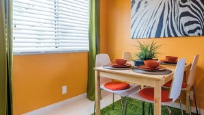 Un coin repas avec une table dressée pour quatre personnes, une œuvre d’art à motifs zébrés accrochée au mur et une fenêtre équipée de stores.
