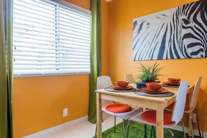 Ein Essbereich mit einem Tisch für vier Personen, einem Wandbild mit Zeprazebra-Muster und einem Fenster mit Jalousien.