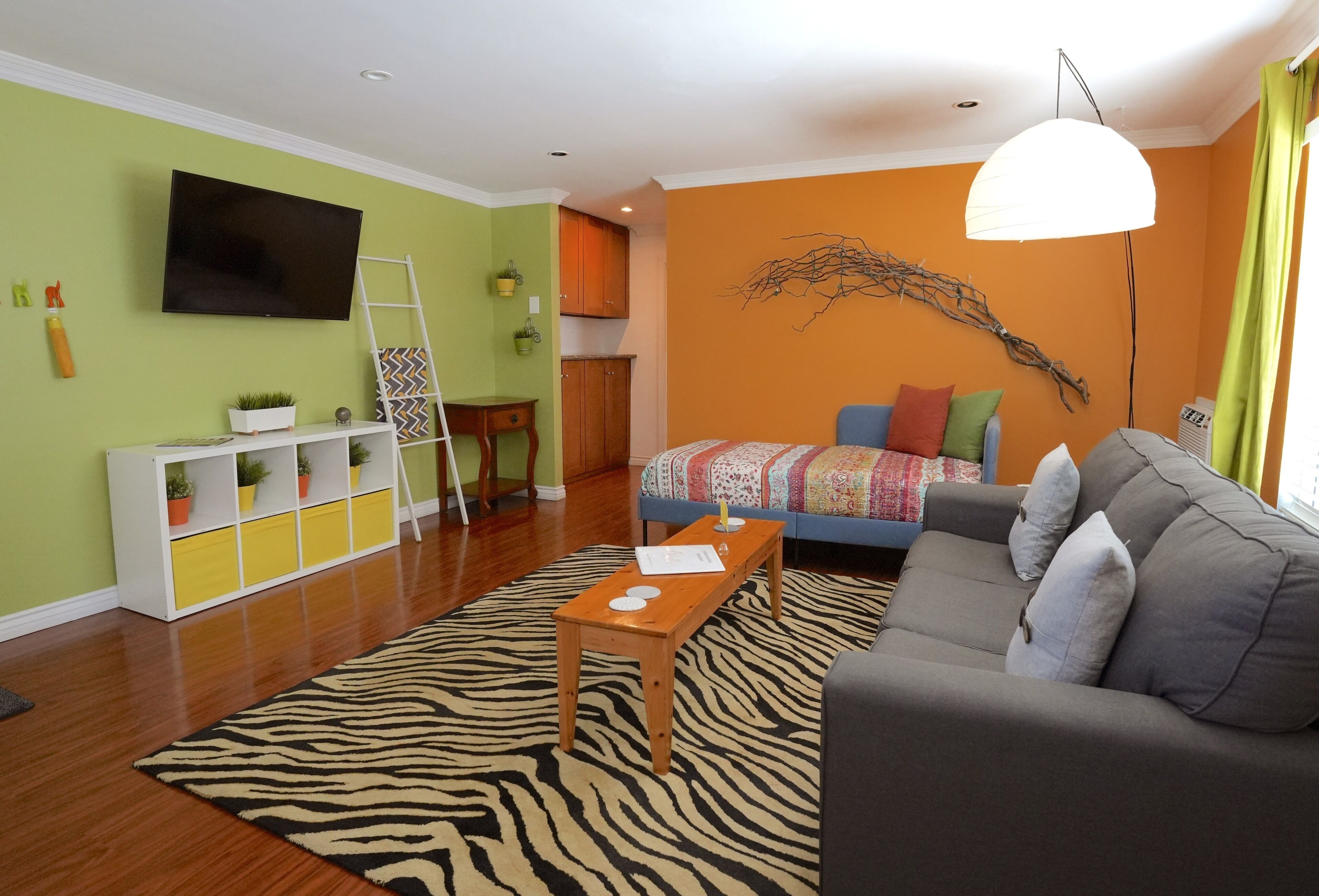 A modern living room with a zebra-patterned rug, a grey sofa, a wooden coffee table, and a television mounted on the wall.