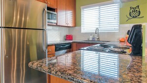 Une cuisine équipée d’appareils électroménagers en acier inoxydable, de plans de travail en granit et d’armoires en bois.