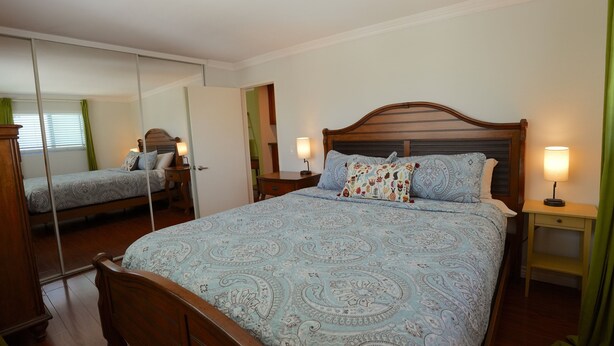 Une chambre à coucher avec un lit double, deux tables de chevet avec des lampes, un miroir et une porte donnant sur une autre pièce.