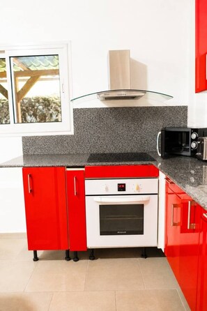 A kitchen with red cabinets, a white oven, and a stainless steel range hood. - Jasmin: Spacious, quiet apartment with a pool for 6 (Le Gosier)