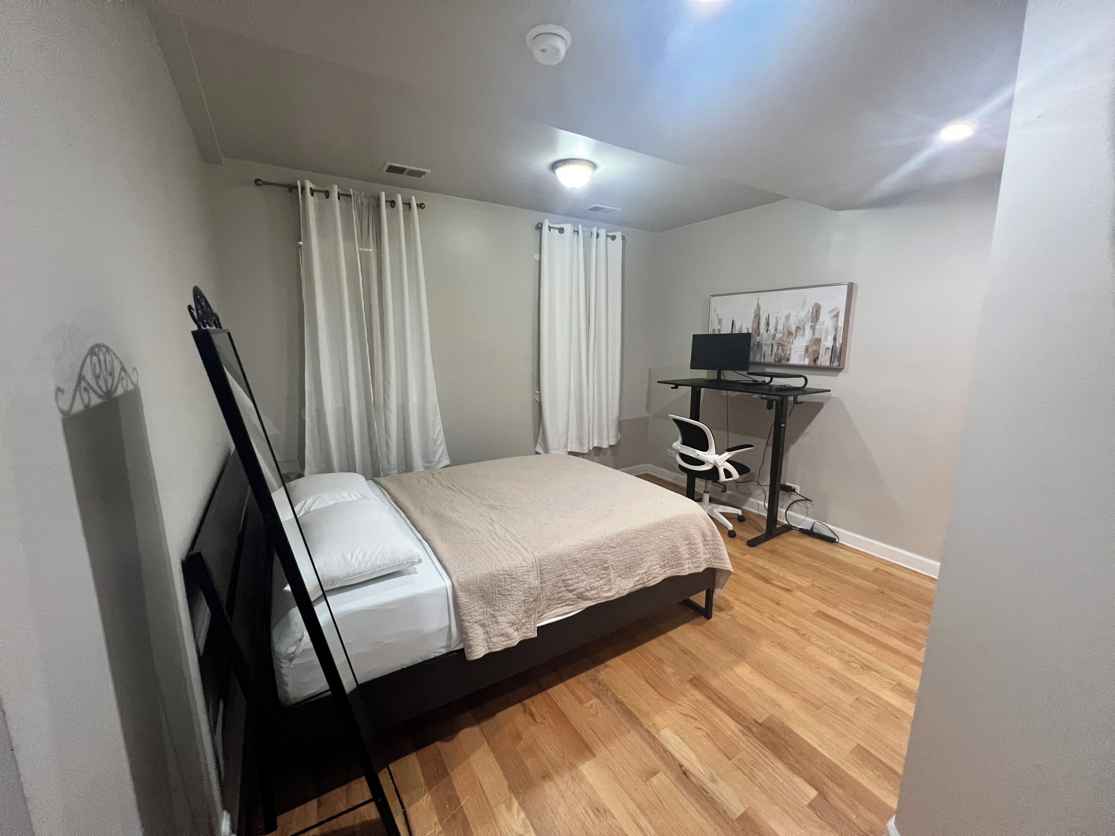 A bedroom with a bed, a desk with a computer, a chair, and a painting on the wall.