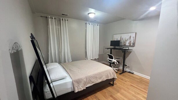 Ein Schlafzimmer mit einem Bett, einem Schreibtisch mit Computer, einem Stuhl und einem Bild an der Wand.