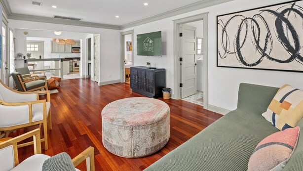A spacious living room with a round ottoman, a green sofa, and a large abstract painting on the wall.