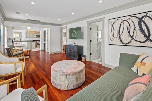 A spacious living room with a round ottoman, a green sofa, and a large abstract painting on the wall.
