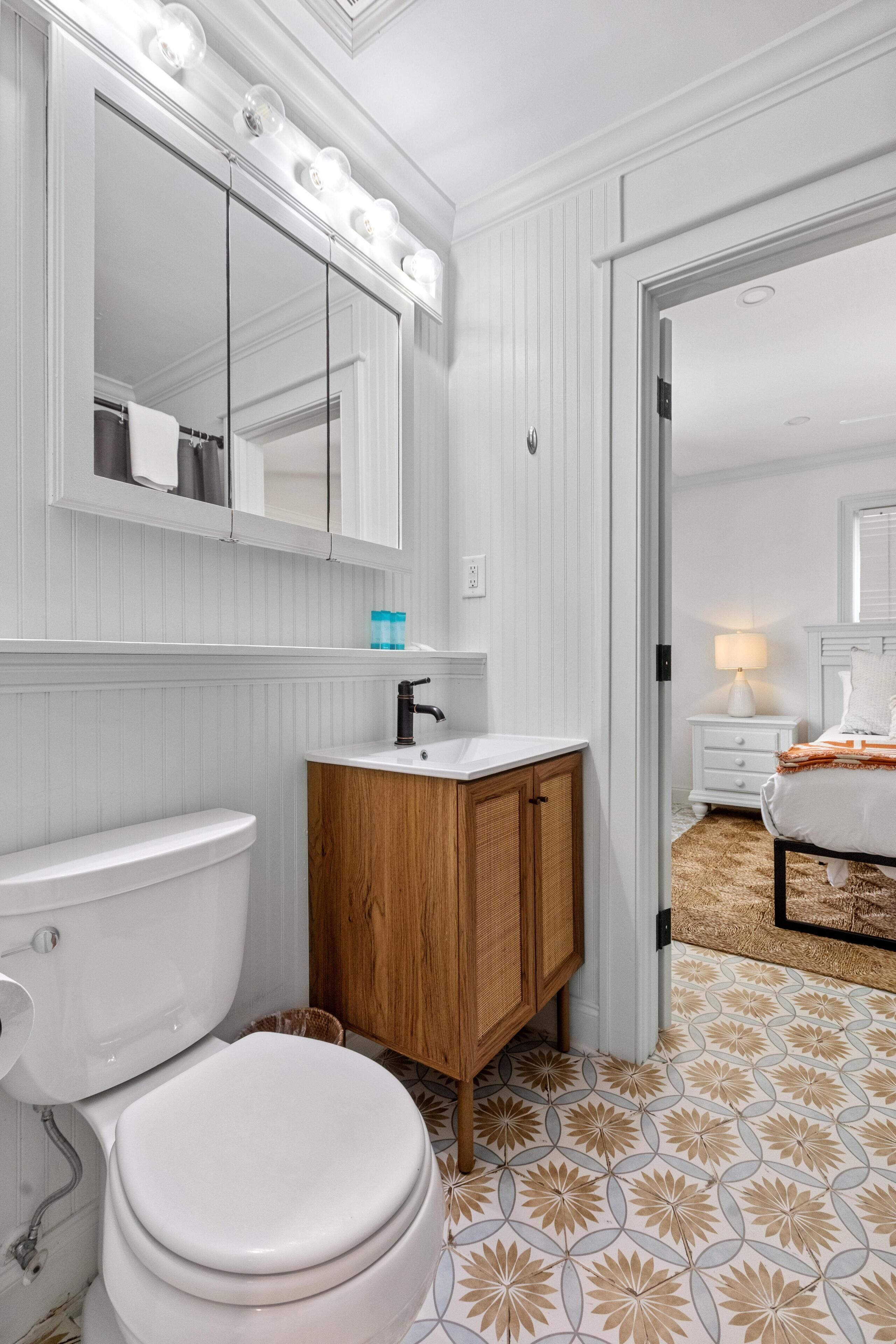 A bathroom with a toilet, sink, mirror, and wooden cabinet.