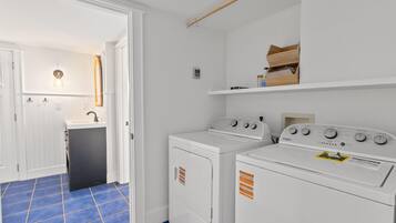 Een wasserette met twee witte wasmachines en drogers, een spoelbak en een vloer belegd met blauwe tegels.