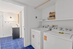 A laundry area with two white washers and dryers, a sink, and a blue-tiled floor. - 1111 Simmons St - MTP (Mount Pleasant)