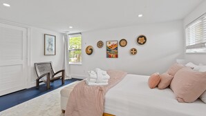 A bedroom with a bed, pillows, a chair, a window, and wall art.