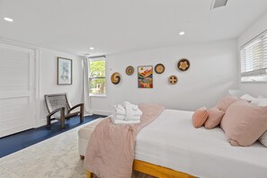 A bedroom with a bed, pillows, a chair, a window, and wall art.
