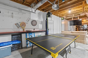 Una mesa de ping pong en una habitación con dardos, una raqueta de tenis y una pizarra con escritura.