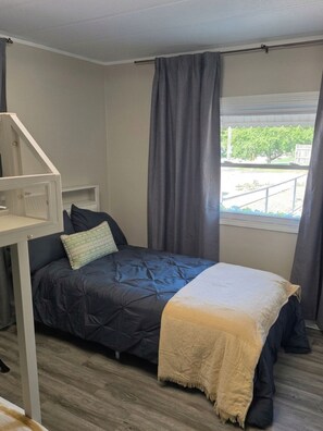 A single bed with a dark blue duvet, a white throw blanket, and a small bedside table with a lamp.
