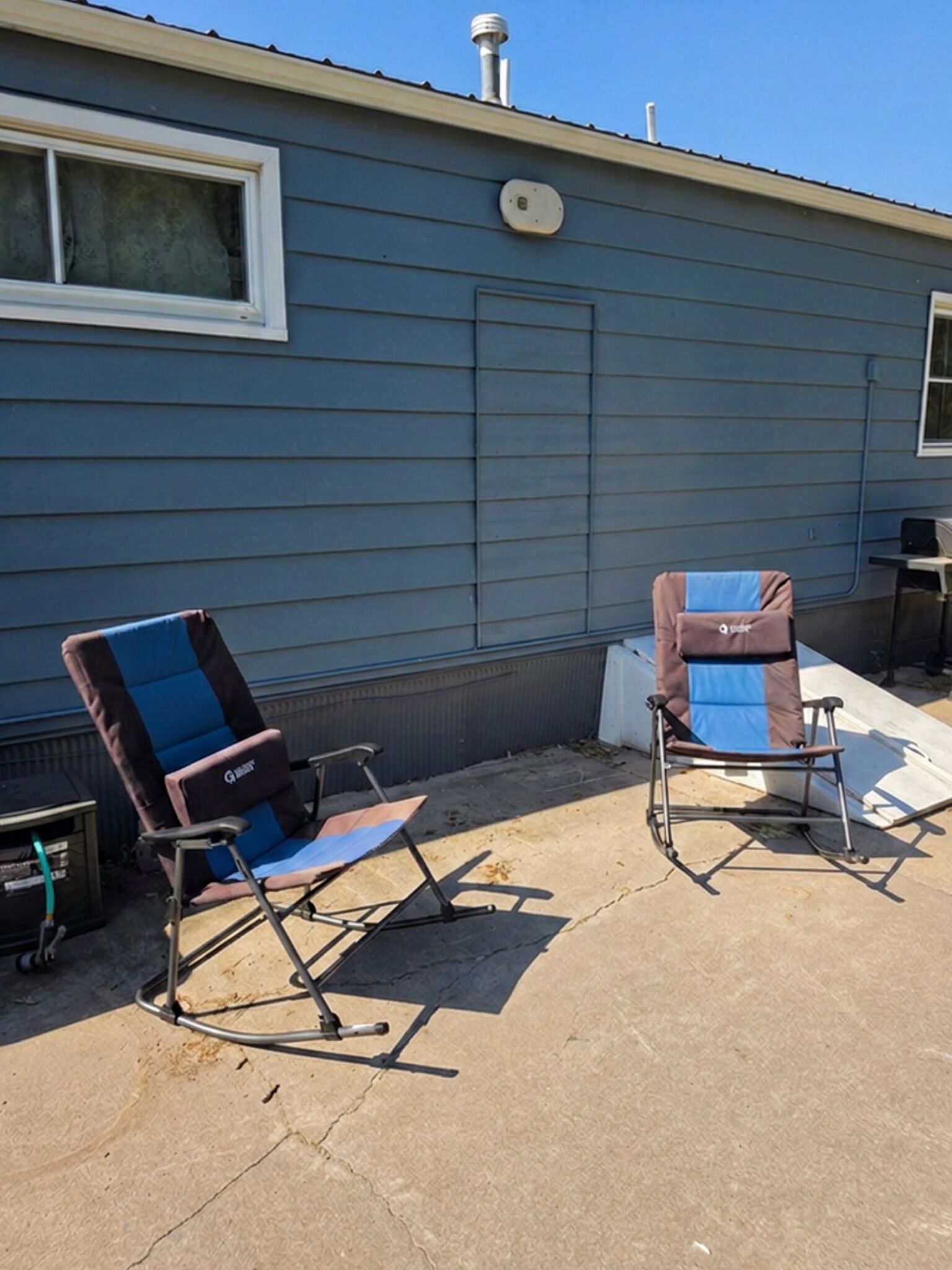 Two folding chairs outside a house with a window and a vent on the wall.