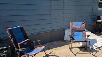 Two folding chairs outside a house with a window and a vent on the wall.