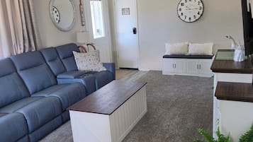 A living room with a blue sofa, a wooden coffee table, a ceiling fan, and two wall clocks.