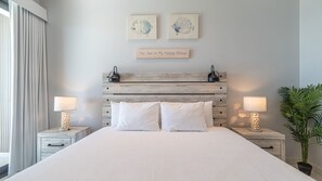 Ein Schlafzimmer mit einem Bett, zwei Nachttischen, einer Wandlampe, einem Topf mit einer Pflanze und zwei Wandbildern.