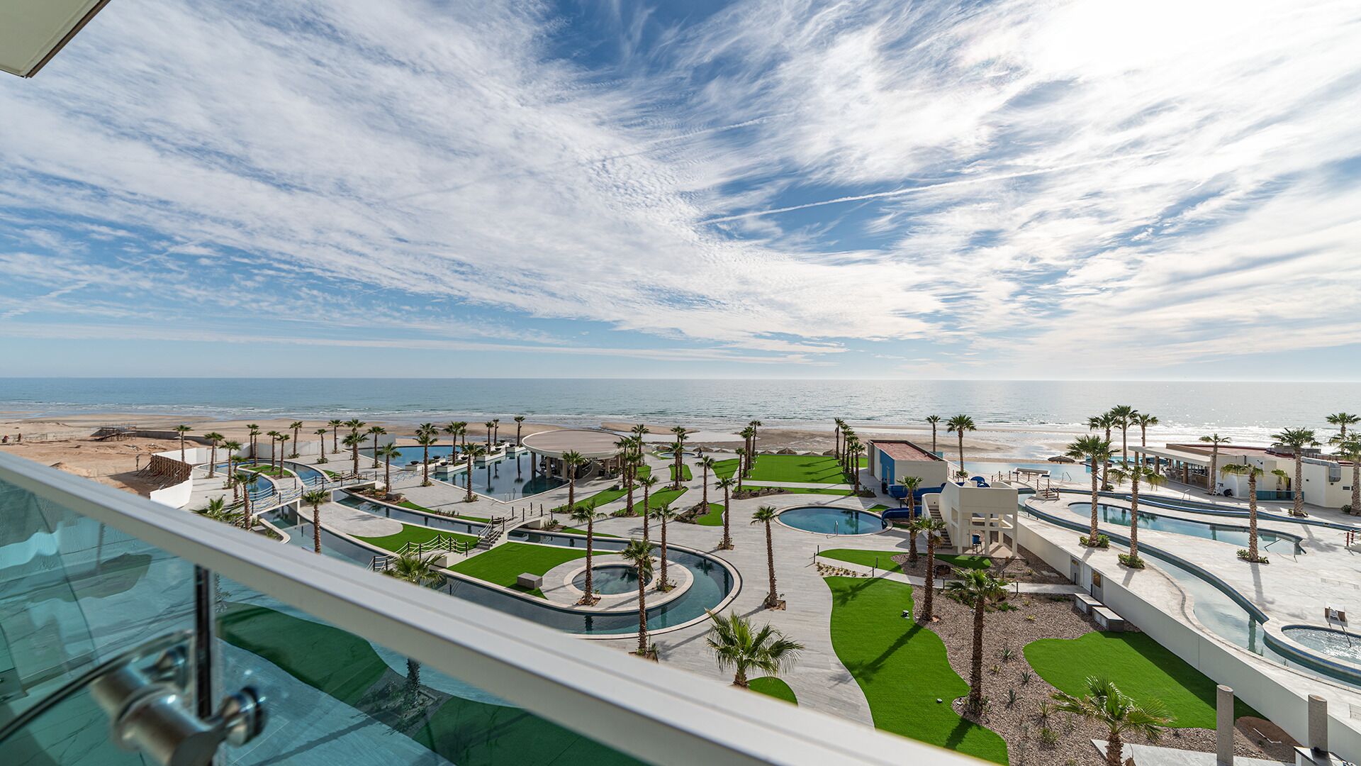 A resort with multiple swimming pools, palm trees, and a view of the beach and ocean.