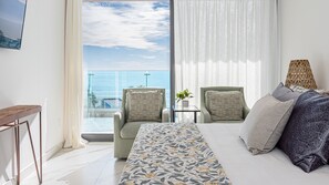 A hotel room with a bed, two armchairs, a small table with a plant, a TV mounted on the wall, and a view of the ocean. - R401 Encantame Soleil – Stunning 3BR Condo with Beachside Views and Spacious Balcony (Puerto Peñasco)