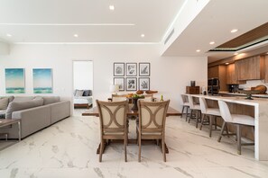 A modern living room with a sofa, dining table, and chairs, a kitchen with wooden cabinets, and artwork on the walls. - R401 Encantame Soleil – Stunning 3BR Condo with Beachside Views and Spacious Balcony (Puerto Peñasco)