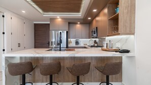 Una cocina moderna con una isla central, taburetes de bar y electrodomésticos integrados.