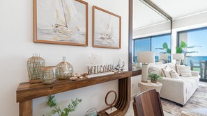 A modern living room with a wooden console table displaying decorative items, a 'WELCOME' sign, and two framed artworks above. - R302: Stunning One Bedroom Beachfront Condo at Encantame Soleil (Puerto Peñasco)