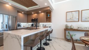 Una cucina moderna con isola in marmo, sgabelli da bar, forno a incasso e angolo caffè.