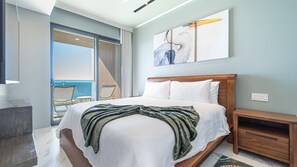 Ein Hotelzimmer mit Bett, Nachttisch, Sessel und Blick auf den Ozean.