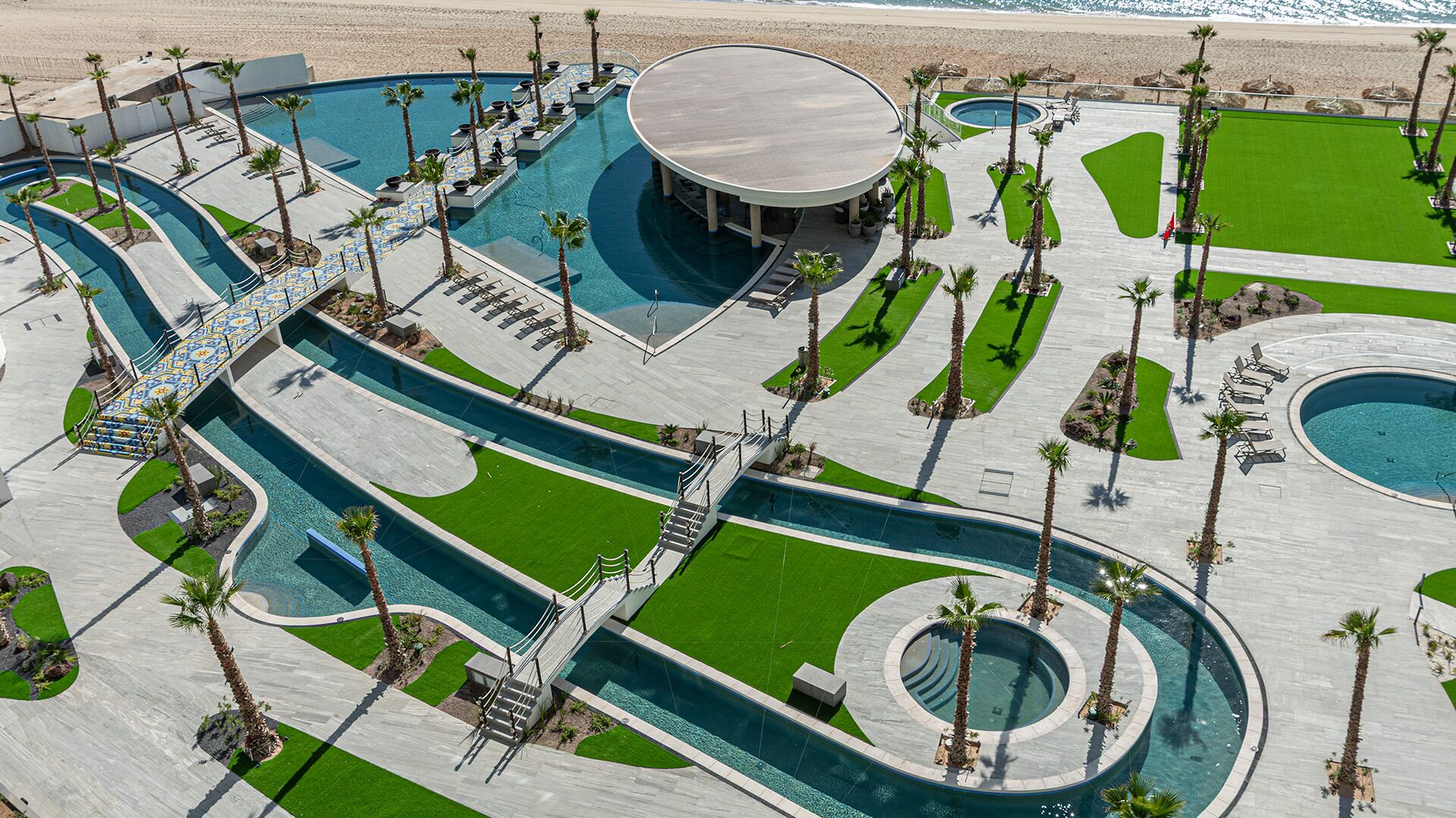 An aerial view of a resort with multiple swimming pools, palm trees, and a beach.