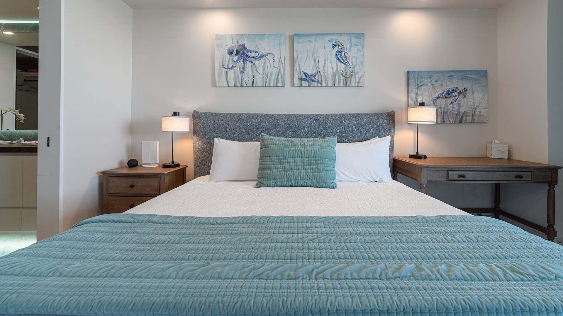 A hotel room with a bed, two bedside tables, a desk, and artwork on the walls.