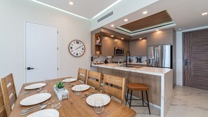 A modern kitchen with a central island, stainless steel appliances, and a dining area with a wooden table and chairs. - R603 Full Unit Luxury Oceanfront Retreat with Stunning High Floor Beachfront Views (Puerto Peñasco)