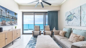 A modern living room with a large window, a ceiling fan, and a view of the ocean. - R603 Full Unit Luxury Oceanfront Retreat with Stunning High Floor Beachfront Views (Puerto Peñasco)