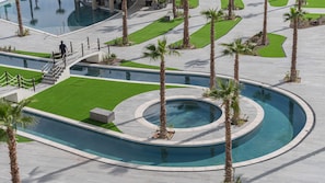 A pool area with a circular water feature, palm trees, and a paved walkway. - Encantame Soleil studio with king bed, 1 bath, for up to 2 adults. (Puerto Peñasco)