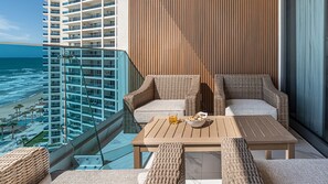 A balcony with wicker furniture, a table, and a glass railing overlooking a beach and ocean. - R1204 Oceanfront 3BR Condo with Stunning Views & Modern Comfort (Puerto Peñasco)