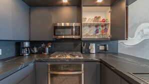 A modern kitchen with a built-in microwave, stove, and oven, a coffee maker, and a shelf with glassware. - R1102 Stylish Beachfront Escape with King Suite and Ocean Views (Puerto Peñasco)