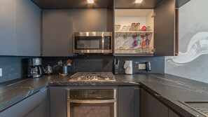 A modern kitchen with a built-in microwave, stove, and oven, a coffee maker, and a shelf with glassware. - R1102 Stylish Beachfront Escape with King Suite and Ocean Views (Puerto Peñasco)