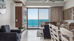 A modern living room with a view of the sea, a ceiling fan, and a large window. - R804 Encantame Soleil 3BR Ocean View Condo with Modern Kitchen and Private Balcony (Puerto Peñasco)